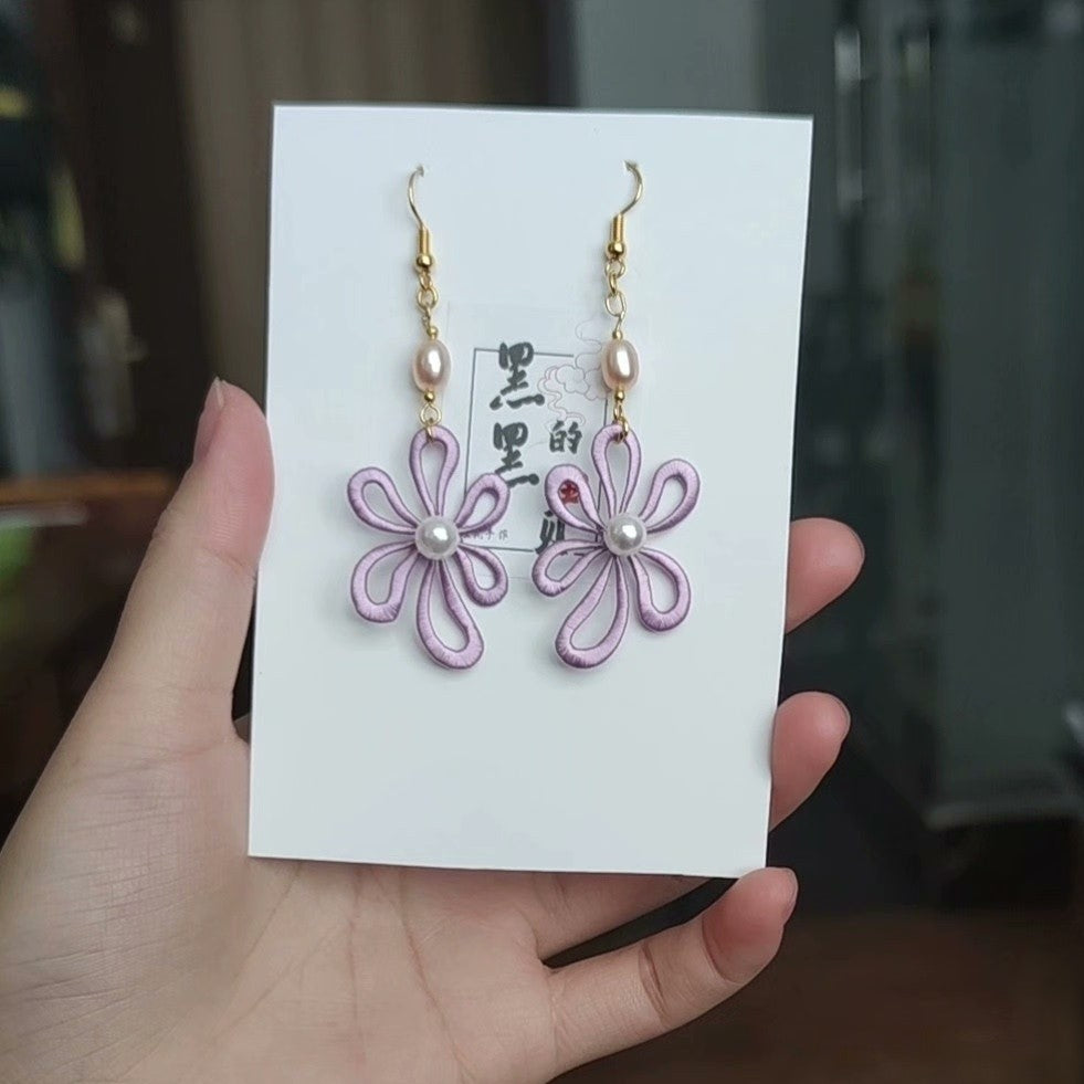A pair of handmade lilac Chanhua flower earrings with freshwater pearls and 925 sterling silver hooks, held on a white card.