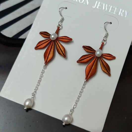 Close-up of a pair of handmade Chanhua maple leaf earrings with a pearl dangle and 925 sterling silver hooks.