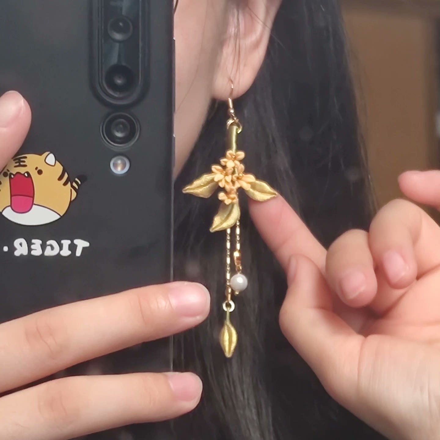 Close-up of a handmade Chanhua flower dangle earring worn by a woman, showing the intricate details of the golden leaves and pearl accents.