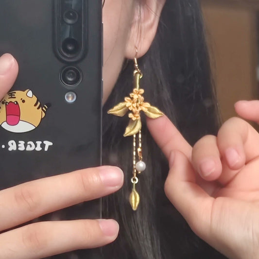Close-up of a handmade Chanhua flower dangle earring worn by a woman, showing the intricate details of the golden leaves and pearl accents.