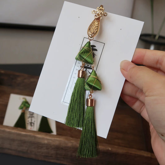 Handmade Zongzi-shaped green tassel earrings on a white card, held by a hand.