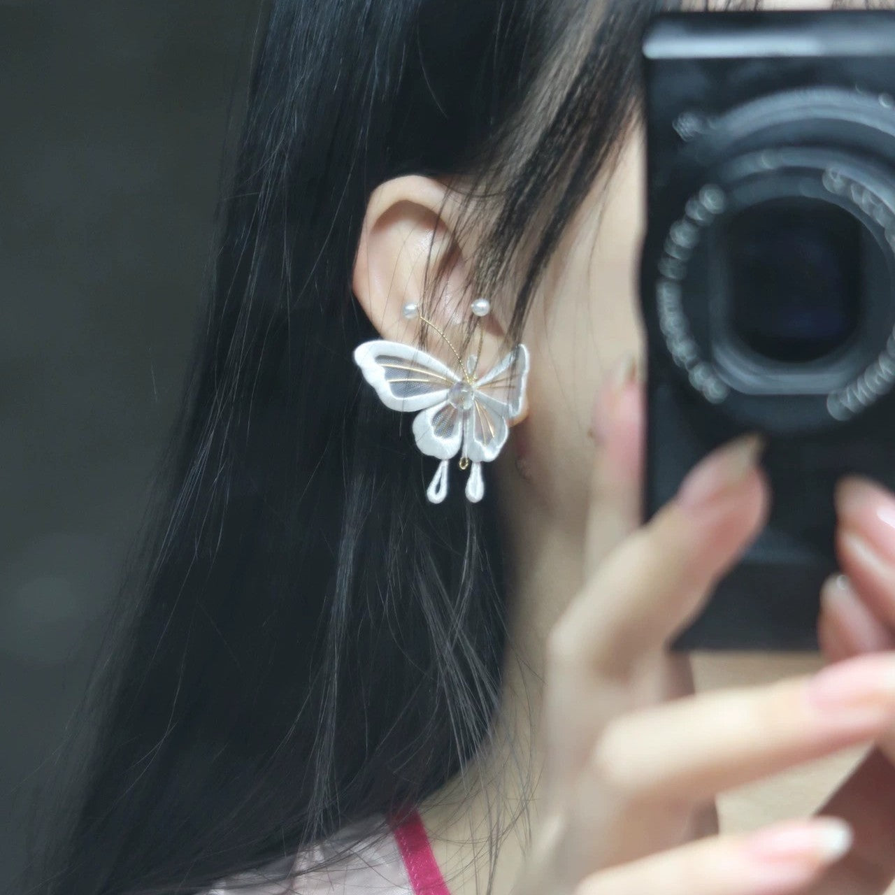 A close-up of a person wearing a handmade Chanhua butterfly earring made of velvet thread, with 925 silver hooks, against a dark background, showing the intricate details of the wing and pearl accents.