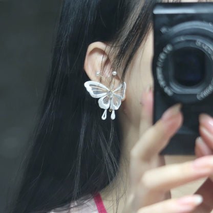 A close-up of a person wearing a handmade Chanhua butterfly earring made of velvet thread, with 925 silver hooks, against a dark background, showing the intricate details of the wing and pearl accents.