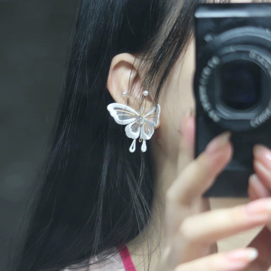 A close-up of a person wearing a handmade Chanhua butterfly earring made of velvet thread, with 925 silver hooks, against a dark background, showing the intricate details of the wing and pearl accents.