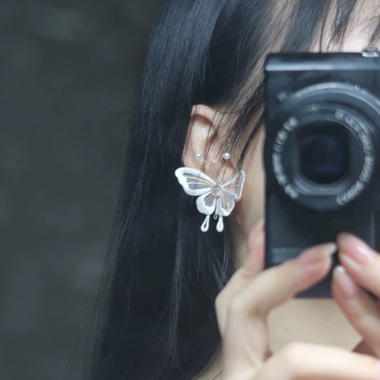 Side profile of a person wearing a delicate handmade velvet thread Chanhua butterfly earring, showcasing its elegant dangle design and how it sits on the ear, with a camera partially visible in the foreground.