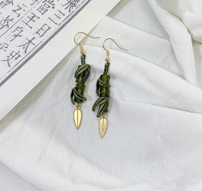 A close-up shot of the handmade bamboo and leaf dangle earrings on a white cloth background with an open book.