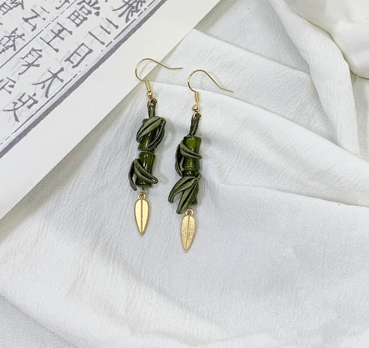 A close-up shot of the handmade bamboo and leaf dangle earrings on a white cloth background with an open book.