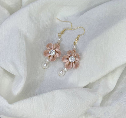 Handmade pink Chanhua flower drop earrings with a sparkling crystal center and pearl accents on a white fabric background.