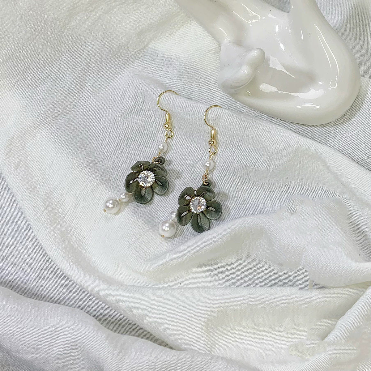 Handmade dark green Chanhua flower drop earrings with a cubic zirconia center and pearl dangles, photographed next to a white ceramic object.
