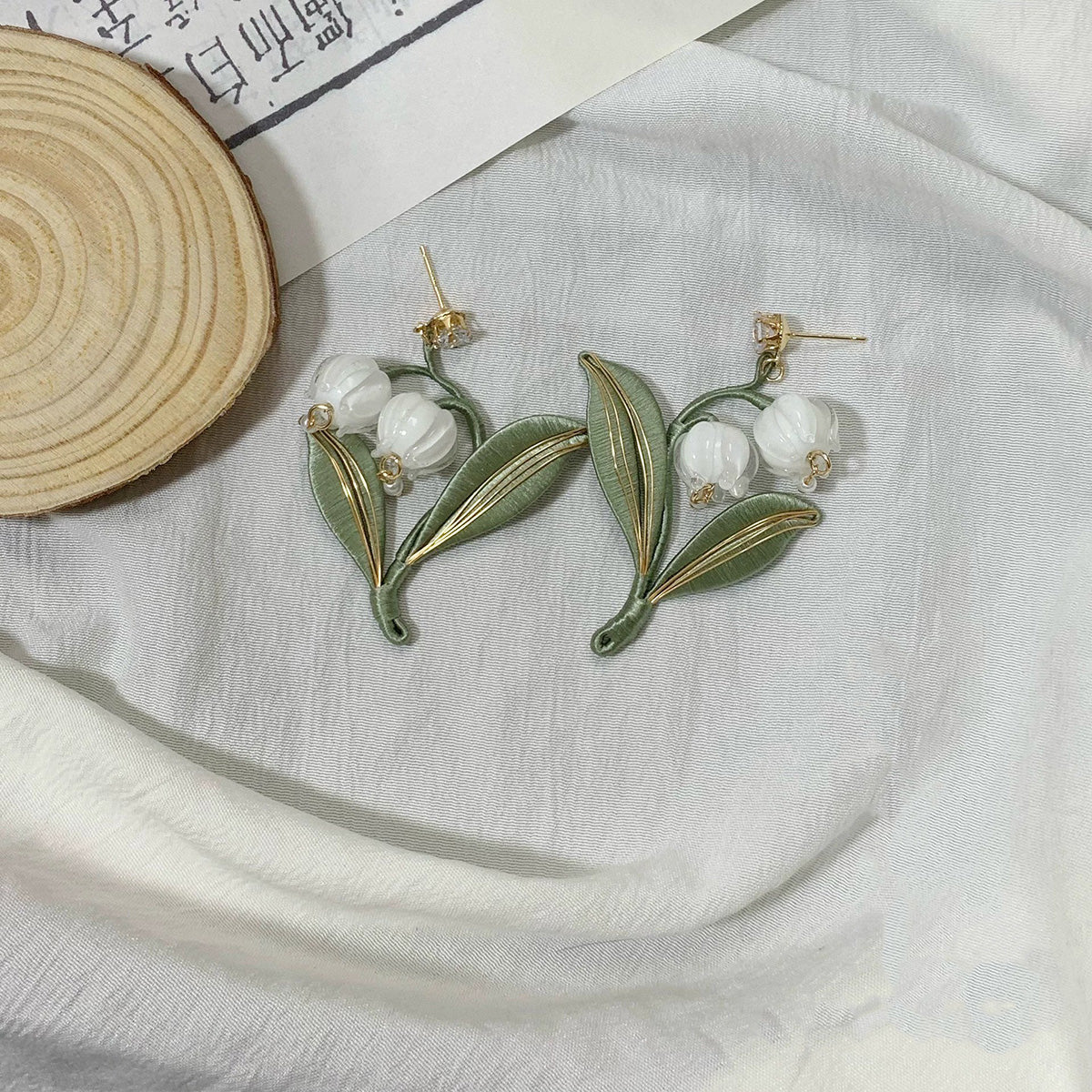 A close-up shot of the handmade lily of the valley earrings with 925 silver hooks on a neutral background, highlighting the detailed craftsmanship.