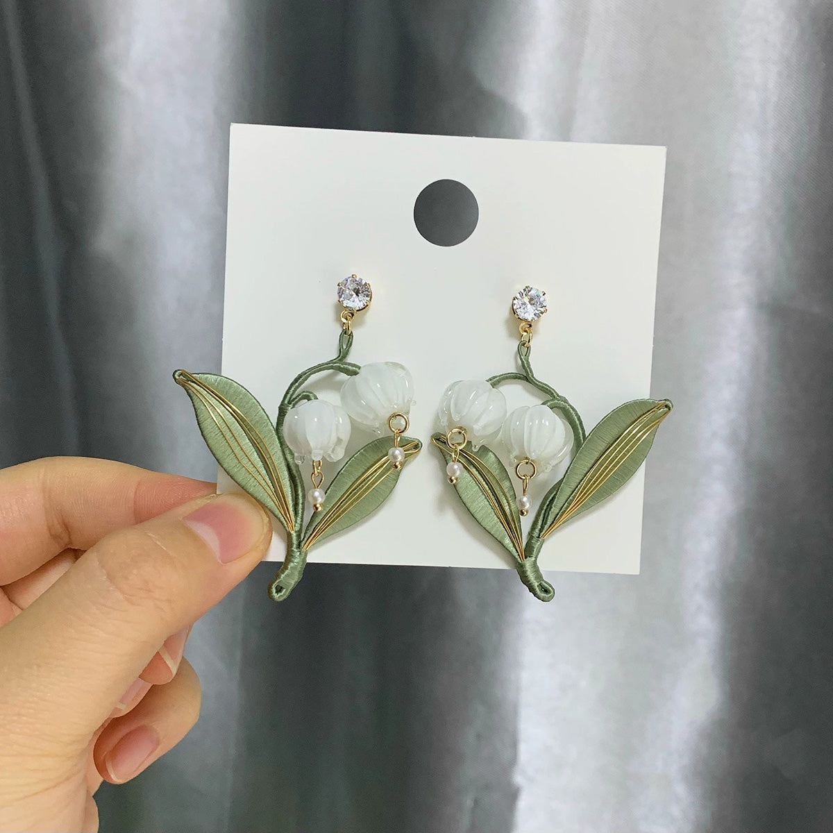 A model's hand holding the delicate handmade lily of the valley earrings, showcasing their size and graceful design.