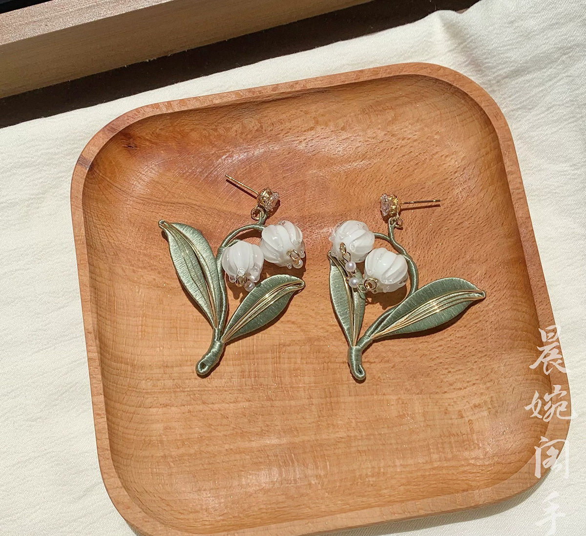 The elegant Chanhua lily of the valley earrings displayed on a rustic wooden tray, emphasizing their natural and artisanal quality.