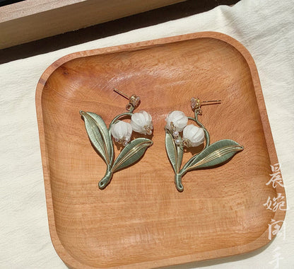 The elegant Chanhua lily of the valley earrings displayed on a rustic wooden tray, emphasizing their natural and artisanal quality.