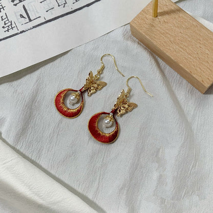 A pair of handmade Chanhua earrings with a golden butterfly and a red embroidered circle.
