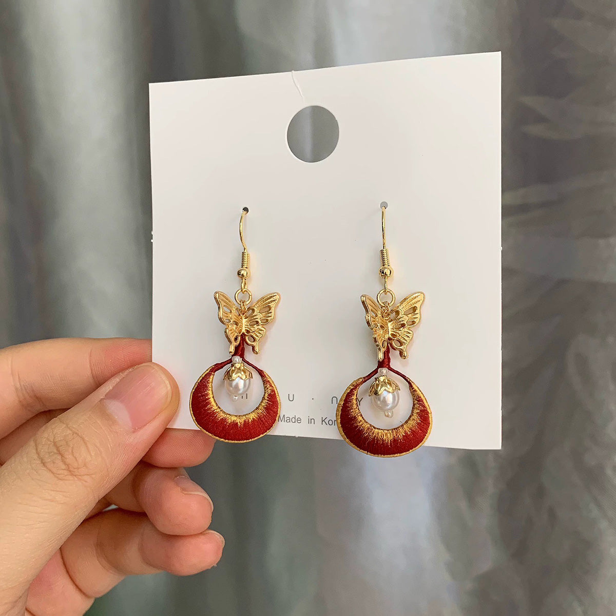 Close-up shot of the Chanhua earrings showing the detailed red embroidery and a dangling freshwater pearl.