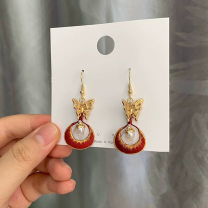 Close-up shot of the Chanhua earrings showing the detailed red embroidery and a dangling freshwater pearl.