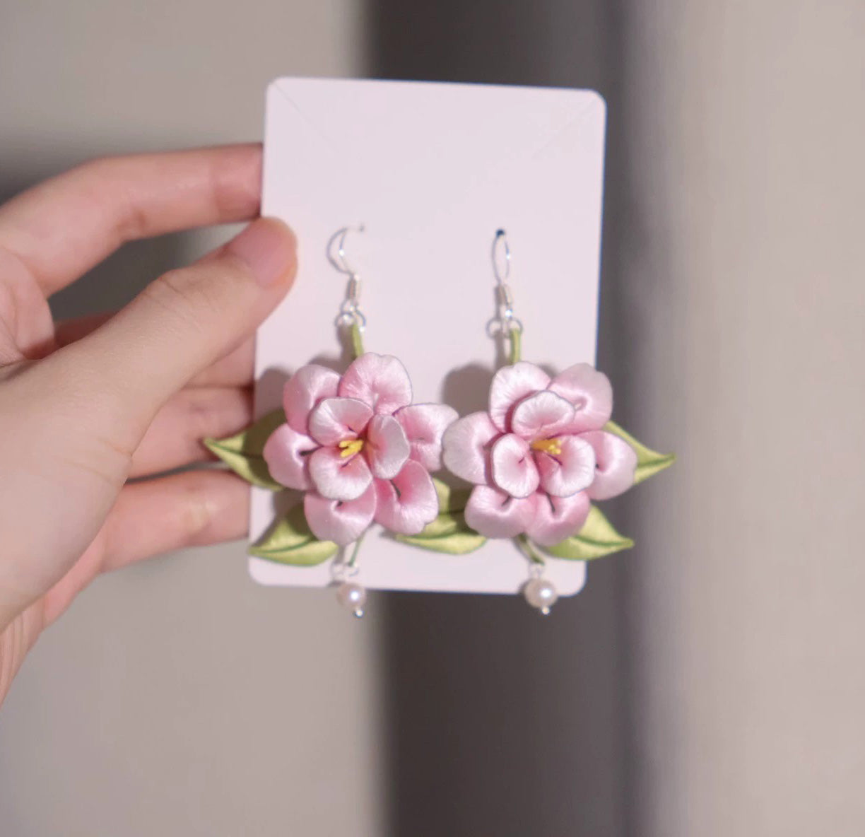 Handcrafted pink silk flower earrings with green leaves and pearl drop, presented on a white card.
