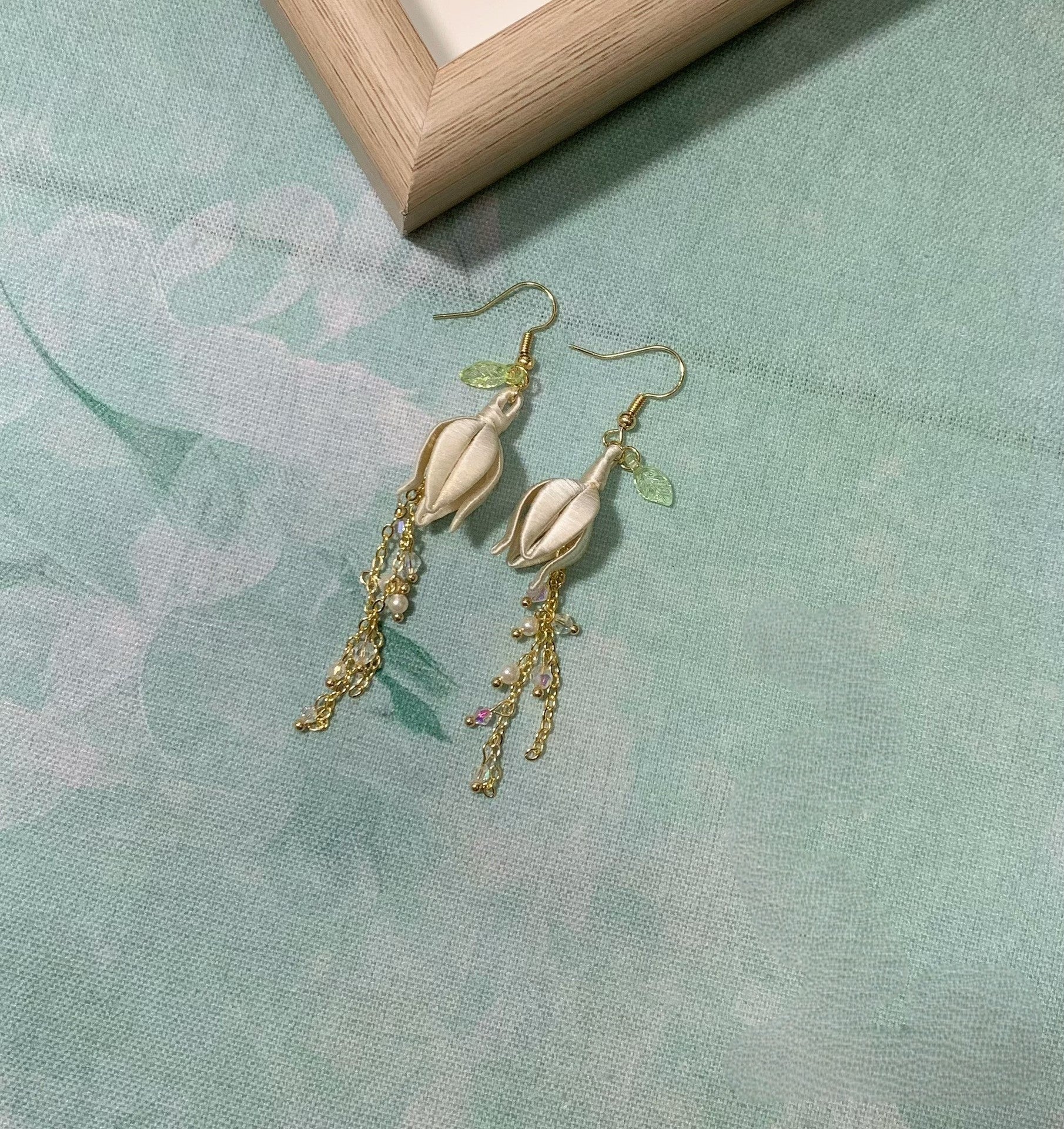 Handmade Chanhua lily of the valley tassel earrings in ivory thread flowers with green leaves, dangling beaded chains and crystals, elegant floral drop earrings