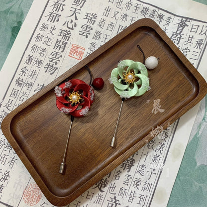 Handmade Chanhua snow-dusted plum blossom brooch set in red and green thread petals with pearl centers, gold leaves, and white snow accents, elegant floral lapel pins