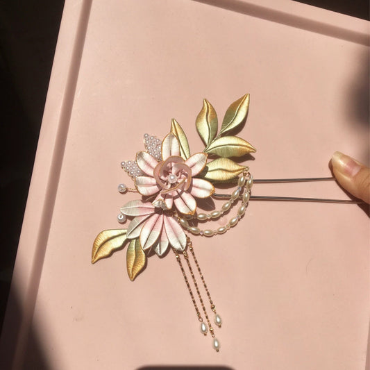 Chanhua handmade pink flower and gold leaf hairpin with pearl chain drape and drop tassels, held against a pink background