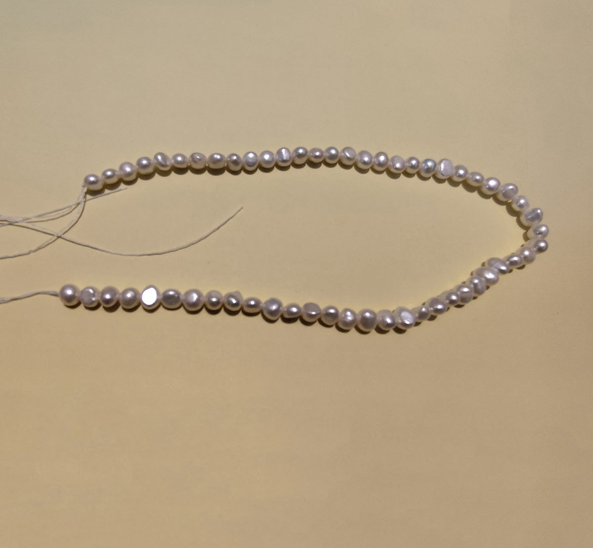 Natural freshwater baroque pearl strand with visible stringing thread for jewelry making.