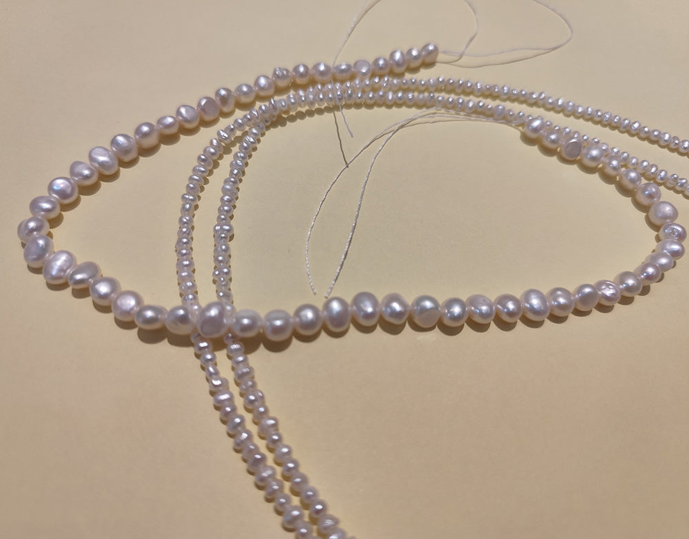 Two long strands of small, natural freshwater baroque pearls laid out on a crafting mat.