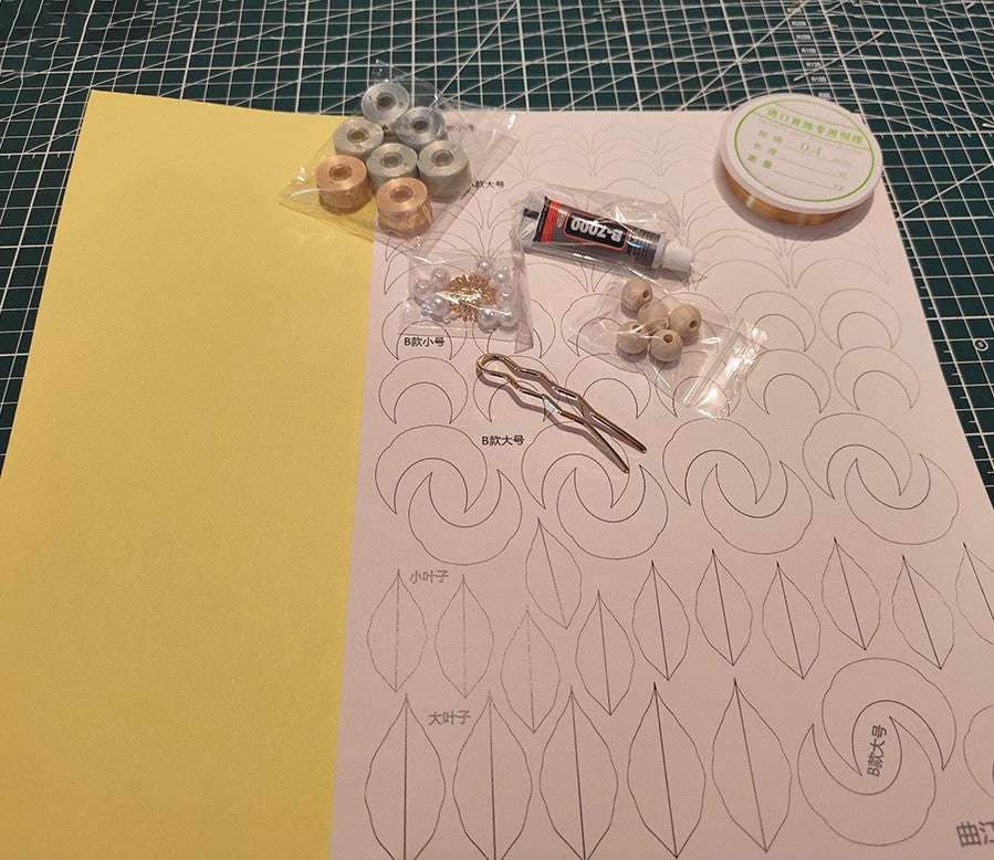 Flat lay of DIY flower craft supplies including velvet thread spools, copper wire, glue, pearl beads, wooden beads, and paper templates on a cutting mat.