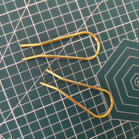 Close-up of two U-shaped alloy hair pins in gold finish, laid flat on a cutting mat, showing detailed craftsmanship for DIY use.