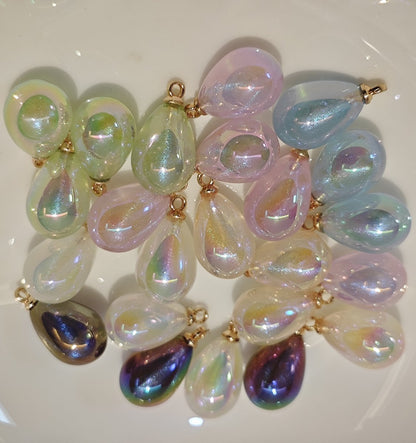 Assorted colors of iridescent galaxy waterdrop charms on a white plate.