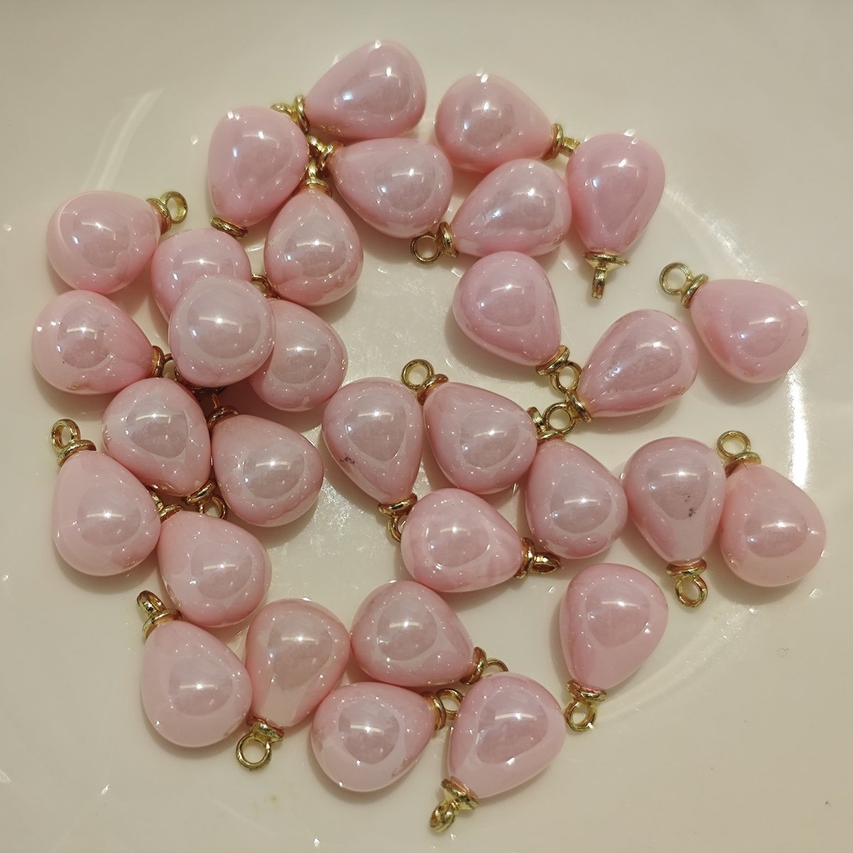 Close-up of small 8x10mm creamy pink teardrop charms with gold loops on a craft cutting mat.