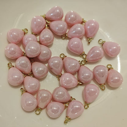 Close-up of small 8x10mm creamy pink teardrop charms with gold loops on a craft cutting mat.