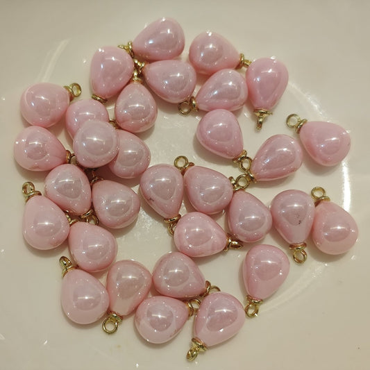 Close-up of small 8x10mm creamy pink teardrop charms with gold loops on a craft cutting mat.