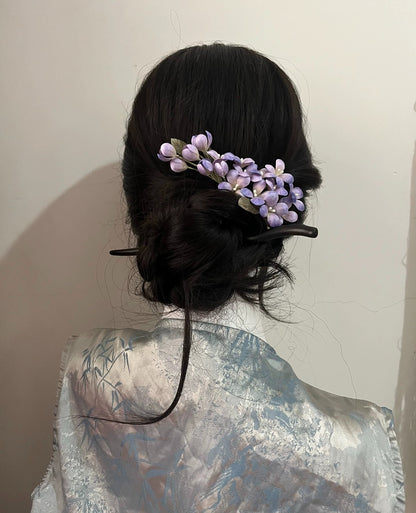 Handcrafted lilac mulberry silk Ronghua flower pin set styled along a dark, woven braid, suitable for a romantic formal look.