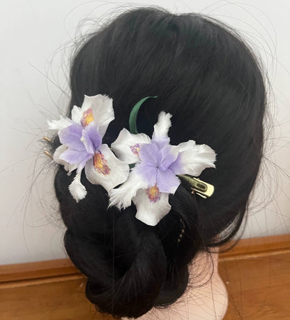 Handcrafted white and lavender mulberry silk Ronghua Iris flower hair pins styled in a dark braided updo, one secured with a clip.