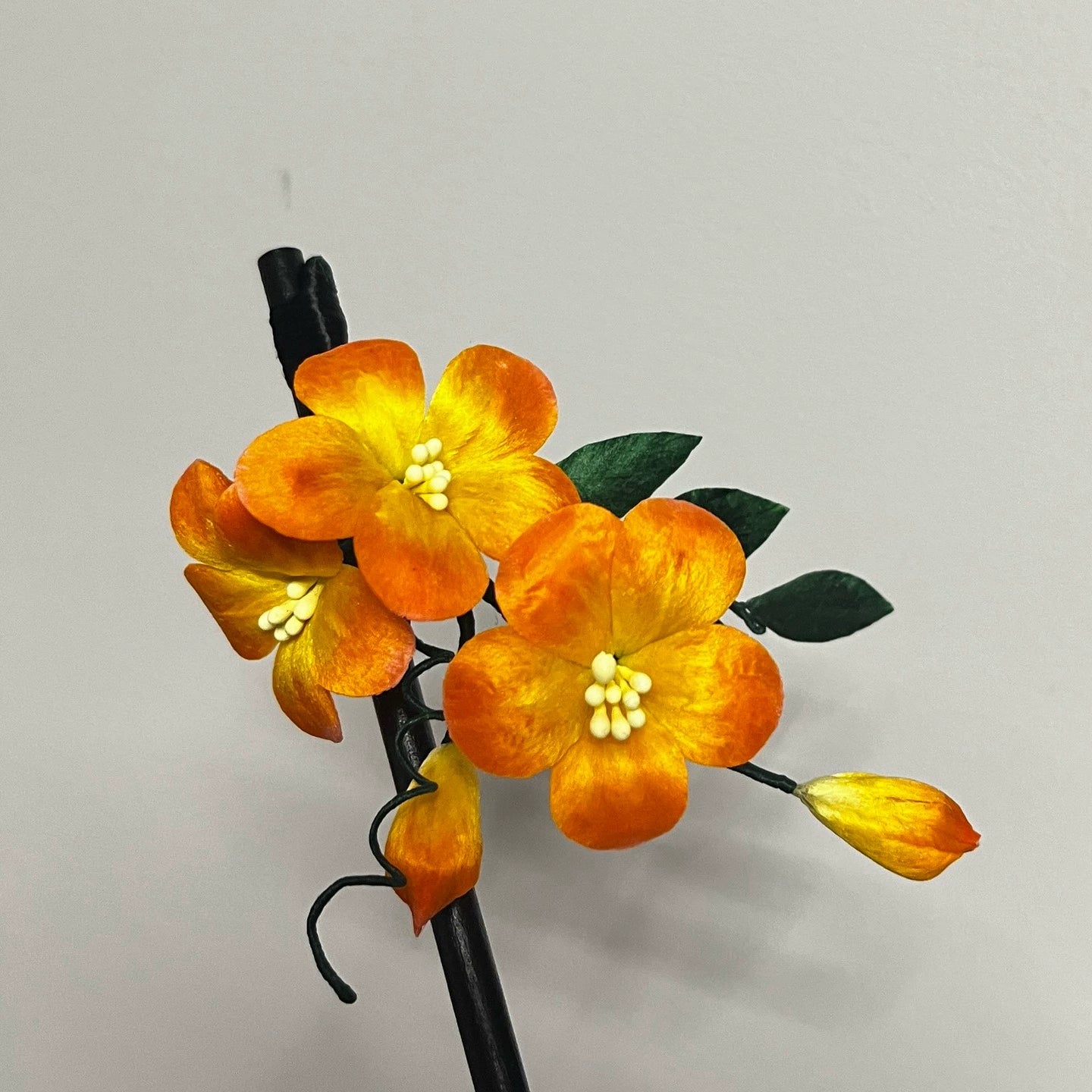 Close-up of a handcrafted orange and yellow mulberry silk Ronghua Trumpet Creeper flower hair stick, showing the vibrant petals and green leaves.