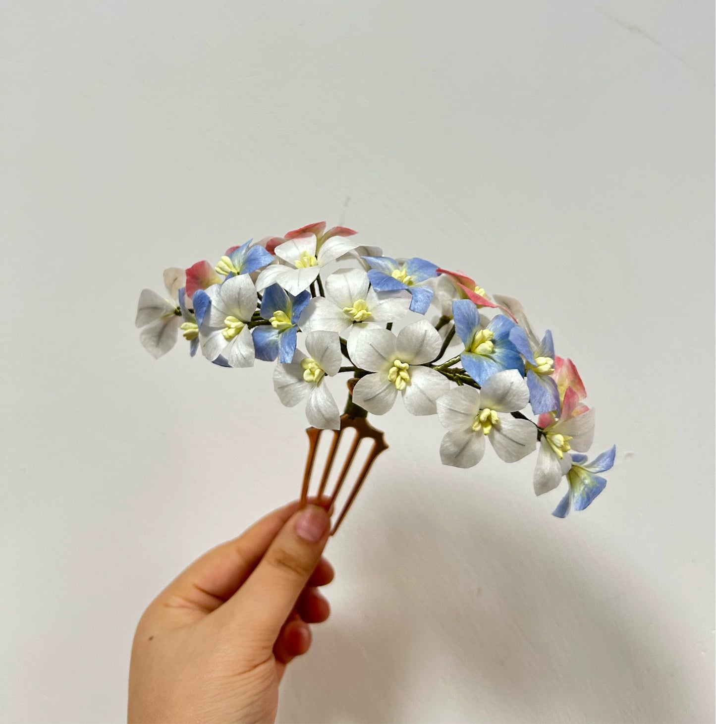 Hand holding a large handcrafted mulberry silk Ronghua hair comb featuring a dense cluster of blue, white, and pink flowers.