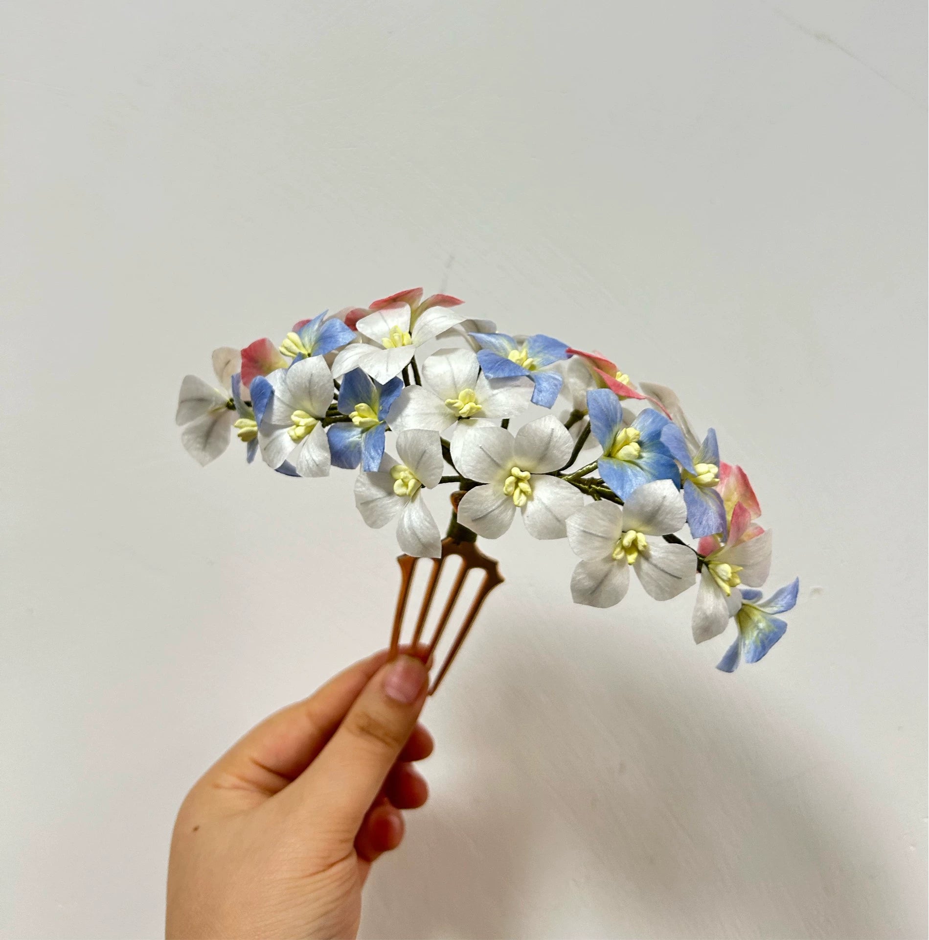 Hand holding a large handcrafted mulberry silk Ronghua hair comb featuring a dense cluster of blue, white, and pink flowers.