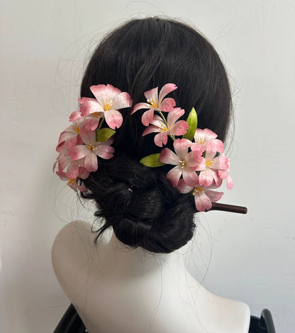 A dark-haired mannequin wearing a large, handcrafted Ronghua cherry blossom hair stick, showing the pink mulberry silk flowers clustered beautifully on a low hair bun.