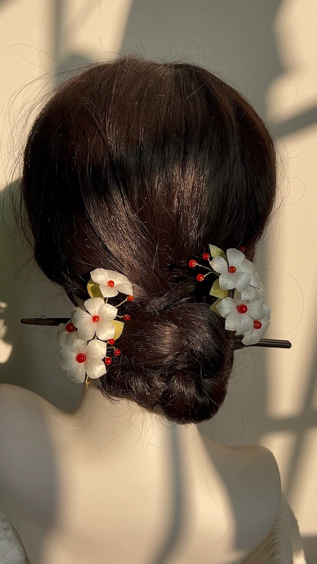 Handmade Ronghua silk hair accessory with small white flowers, red beads, and green leaves secured in a dark hair bun.