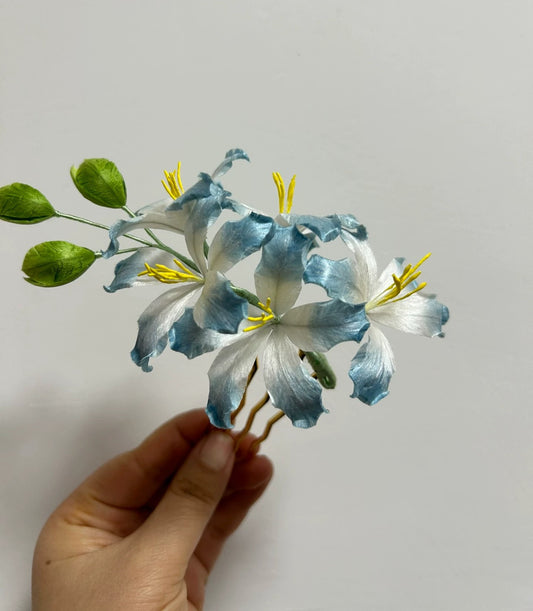 Hand holding handmade blue bauhinia Ronghua silk flower hair comb showing detailed petals and yellow stamens