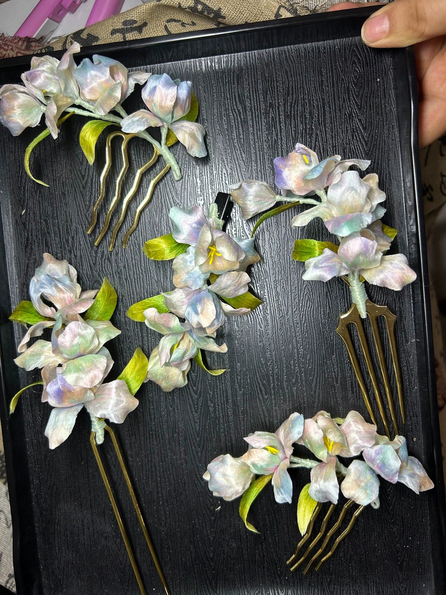 Handmade Ronghua iris flower hair combs in colorful pastel shades, crafted from natural mulberry silk, displayed on a black tray