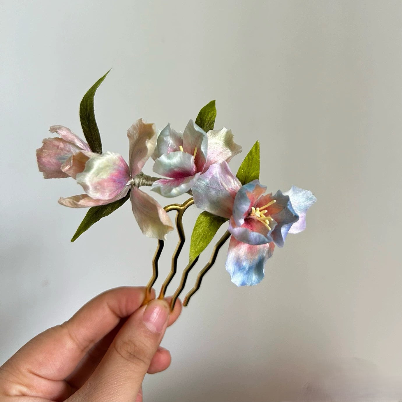 Close-up of handmade gradient color iris flower hair comb in natural silk thread held in hand.