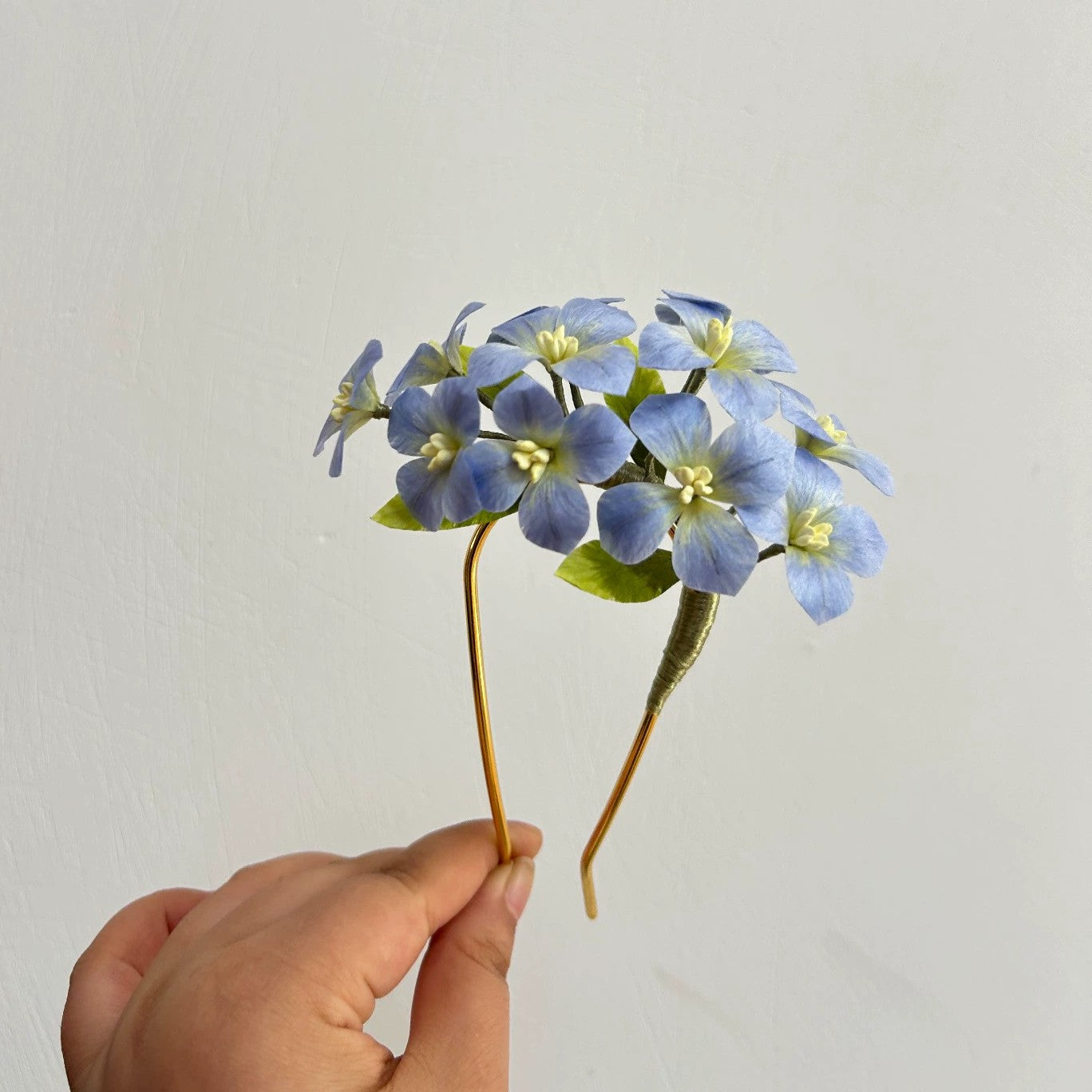 Close-up of handmade blue hydrangea flower hair stick in natural silk thread held in hand.