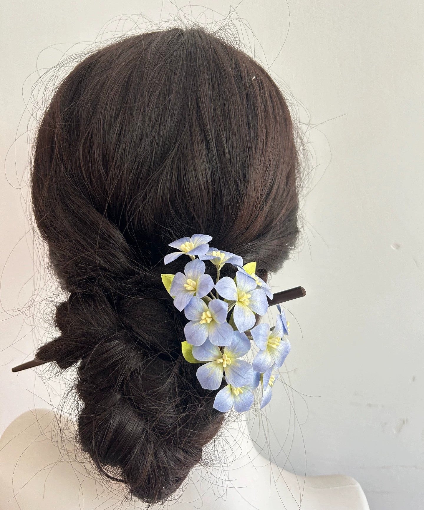 Rear view of blue silk hydrangea flower hair stick in bun hairstyle on mannequin.