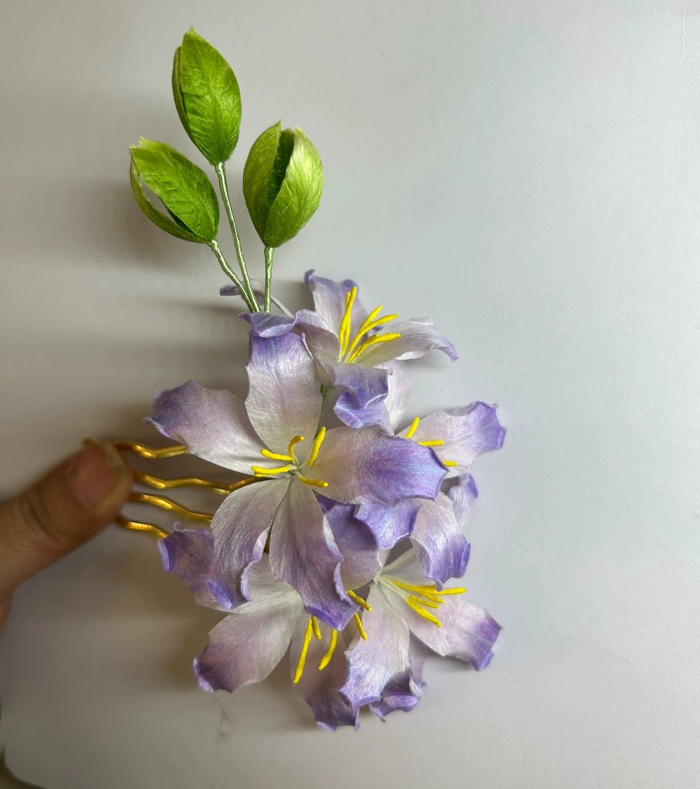 Close-up of handmade purple bauhinia flower hair comb in natural silk thread held in hand.