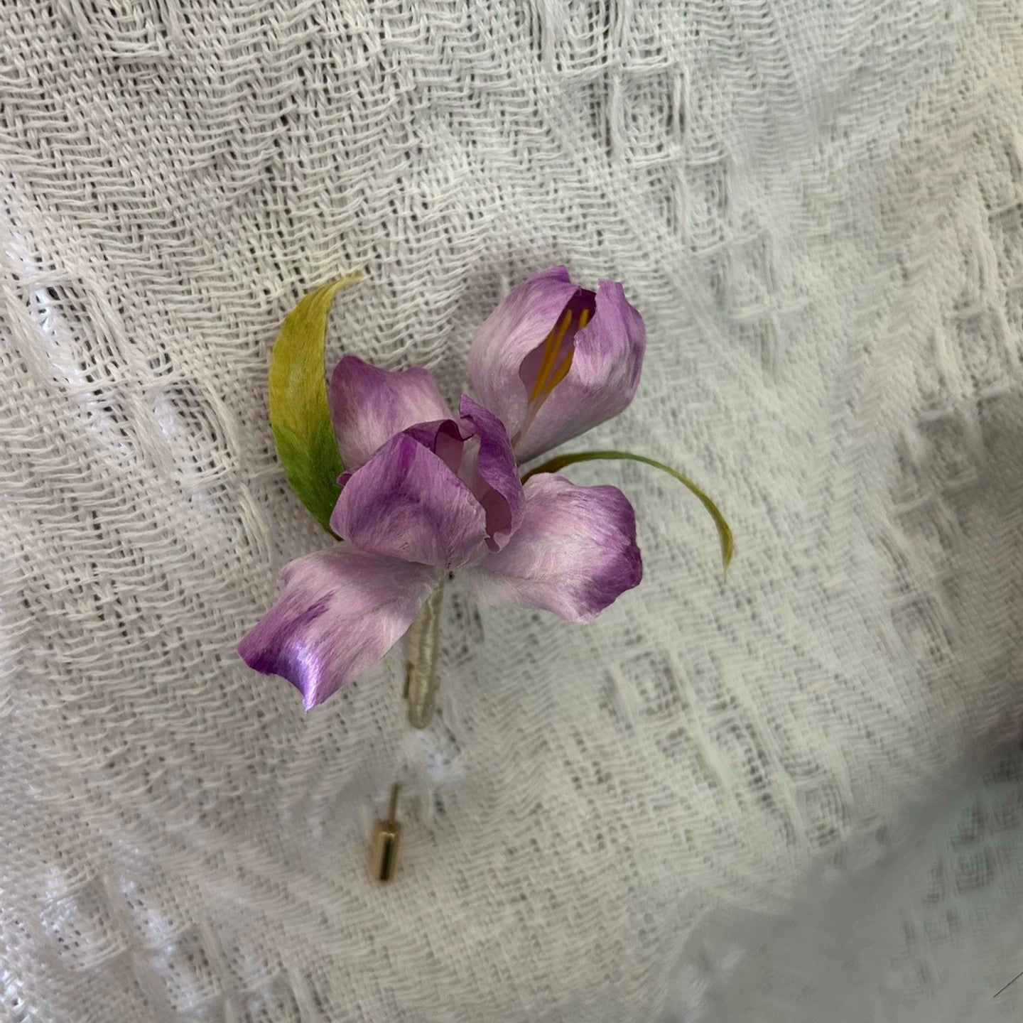 Close-up of handmade purple iris flower brooch in natural silk thread on white fabric.