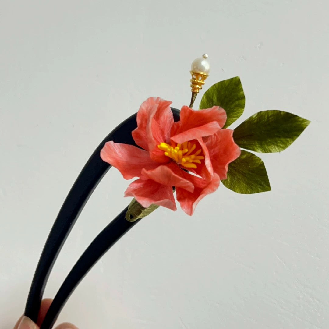Handheld close-up of handmade pink Ronghua silk camellia dual-purpose hairpin and brooch with pearl accent