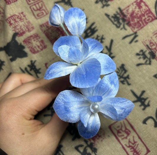 Handheld close-up of handmade Ronghua blue hydrangea hair comb crafted from natural mulberry silk thread with freshwater pearls