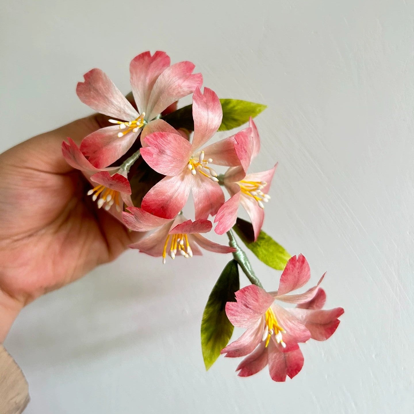 Handheld close-up of handmade Ronghua soft pink cherry blossom flexible hair stick made with natural mulberry silk thread