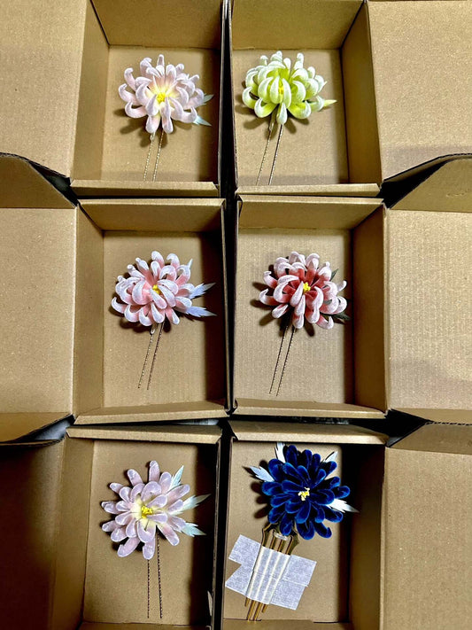 Collection of handmade Ronghua chrysanthemum hair pins in pink, yellow-green, blush, and navy mulberry silk displayed in kraft boxes